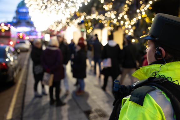 Police officer looking over people shopping. Christmas lights shining in the background.