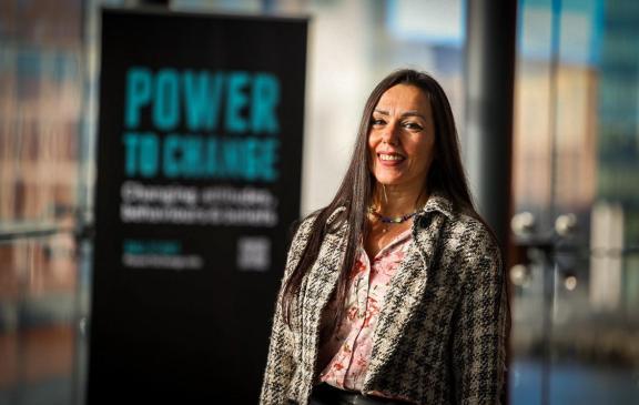 Photograph of Eva Komuves in front of a 'Power to Change' sign